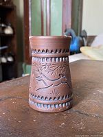 Front view of the brown Mohawk pottery vase showing carved bird and foliage designs and decorative patterned bands along the top and bottom edges.