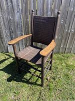Front view of the antique wooden armchair showing woven seat and backrest with wooden armrests.