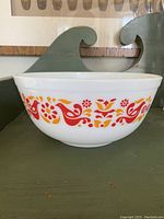 Side view of the Pyrex bowl showing the colorful red and orange Friendship pattern of birds and flowers on white opaque glass.