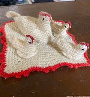Photo of four crochet nesting chickens on a square crochet doily with red trim on a wooden surface.