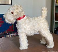 Side shot of white mohair stuffed dog with red collar on a table showing profile details, eyes, and tail.