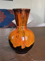 Front view of the vintage orange drip glaze bud vase showing the bulbous body and narrow neck with vibrant orange glaze dripping down over a black glossy finish.