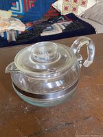 Side angle view of the clear glass Pyrex Flameware teapot showing the handle and metal band.