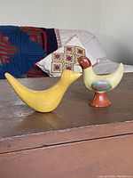 Overview photo of two vintage redware pottery birds on a wooden surface with cushions in background
