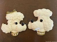 Front view of the two white chalkware poodle dog wall hangings with gold collars, showing detailed textured fur, black noses, one with a gold bow.