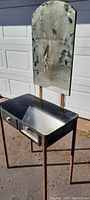 Full view of 1930s standing hair salon station showing steel frame, glass mirror, reflective metal top, and drawer knobs.
