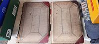 Photo showing the front covers of two large ledger books with textured, patterned covers and leather binding corners, displaying wear and discoloration with age.