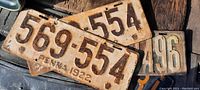 Photo showing several license plates stacked, highlighting worn and rusted 1922 pair numbered 569-554.