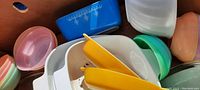 Close-up of pastel-colored small pudding bowls, blue Pyrex container, plastic bowls and lids, and white Pyrex refrigerator dishes with yellow lids.