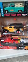 Photo showing side view of three diecast toy vehicles in original boxes: green 1955 Pickup Truck Bank, yellow Coca-Cola delivery truck, red and black NASCAR Stock Car