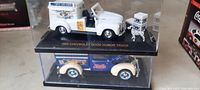 View showing the white 1953 Chevrolet Good Humor truck in original display case on top, and the dark blue Pepsi Cola truck in display case below.