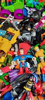 Close-up of Batman, Superman, Robin, Aquaman, and other assorted action figures with a green and pink toy car visible in the background.