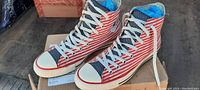 Side and top view showing the American flag striped design on high top Converse sneakers with white laces and rubber soles.