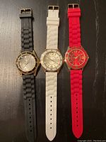 Three ladies silicone band watches in black, white, and red colors, arranged side by side on a black surface.