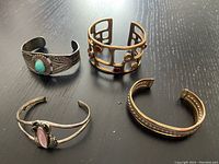 Four cuff bracelets displayed on a dark surface, showing front view and stone details.