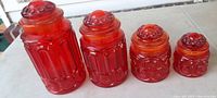 Photograph showing the four vintage red glass canisters from front view with matching lids on a table.