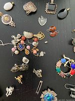 Photo showing assorted jewelry including pins, earrings, a heart pendant, and decorative bracelets on black background.