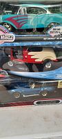 Photo shows three diecast toy cars in original packaging including a teal and white 1967 Chevrolet Bel Air with red flames, a red and cream Ford Hot Rod with exposed engine, and a blue 1948 Chevrolet Fleetline in a clear box.
