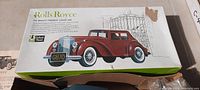 Full-color illustrated box for a vintage Rolls Royce toy model kit showing a red car with license plate GB70 and an elegant gate backdrop. The box shows some edge wear and damage on the top right corner.