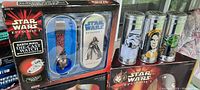 Photo showing the Darth Maul die-cast watch in blue display case and three collectible Star Wars cans featuring Stormtrooper, Obi-Wan Kenobi, and Yoda