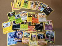 Photo displaying approximately 45 Pokémon trading cards spread out on a surface. Cards include various Pokémon characters and energy cards, showing front design.