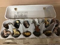Eleven Wade ceramic tea figurines arranged inside a recycled egg carton. Figurines vary in animal shapes and colors, including a Gingerbread Man.