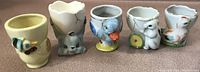 Six vintage ceramic egg cups with various animal designs lined up on a brown surface