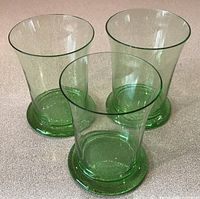 Three green Czech drinking glasses grouped together, showing their flared shape and transparent green glass.