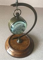 Front angle showing the brass and glass clock mounted on the curved brass arm with wooden base.