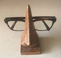 Front view of the hand carved mahogany eyeglass stand holding a pair of glasses, showing wood grain and nose-shaped design.