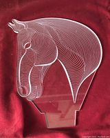 Front view of the clear plexiglass horse head with white etched lines showing contour details of the horse face and mane on a red background.