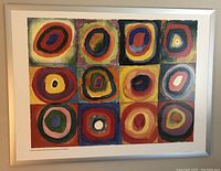 Framed abstract print showing a grid of twelve colorful squares each with concentric rings, the frame is white and modern.