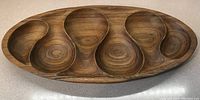 Top-down view of a large teak serving tray with five distinct rounded compartments showing natural wood grain and a smooth finish.