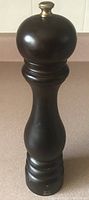 Full view of the 11 inch tall dark wooden Peugeot pepper grinder with classic shape and metallic top knob.