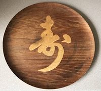 Front view of round teak tray with gold Japanese calligraphy symbol and visible wood grain.