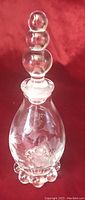 Full view of the vintage glass perfume or rosewater bottle showcasing the stacked round stopper and bulbous body with pinwheel etched floral design.