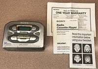 Front and top view of Sony WM-FX491 Walkman cassette player with AM/FM radio function on a brown surface alongside warranty and instruction booklets.