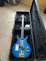 Blue electric bass guitar in its plush-lined black case, showing the body and headstock with four strings and pickups.