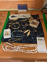 Overview of lot items displayed on a black fabric mat; shows necklaces, bracelets, earrings, pins and charms