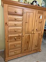Front view of a natural wood finish armoire dresser with seven drawers on the left and two paneled doors on the right.