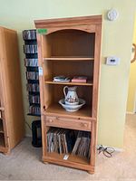 Front view of tall Broyhill wooden bookcase with three shelves and a drawer, containing decorative jug and saucer. Shows natural wood finish and moderate wear.