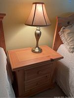 Wood night stand topped with a brushed nickel lamp, positioned between beds with bedding visible.