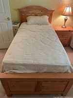 Front view of wooden twin bed with headboard, mattress covered with beige patterned bedding and pillow on top.