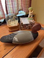 Carved red drake head duck in foreground with glass snow globe containing horse carriage and child figurine in background