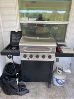 Full front view of Char Broil grill including opened doors, controls, and propane tank beside it on the floor.