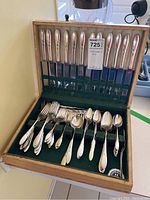 Full wooden box opened to show the entire cutlery set including knives lined vertically, forks and spoons arranged horizontally inside green velvet slots.