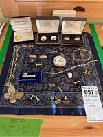 Overhead view of assorted cufflinks, bracelets, pocket watch, necklace, tie bars, rings and brooches laid on patterned cloth