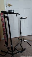 Photo showing both guitar stands side by side; one single guitar stand with adjustable height and padded neck support, and one larger triple guitar stand with three padded arms to hold guitars.