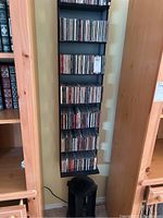 Tall black metal rack against the wall full of assorted music CDs in jewel cases on multiple shelves.