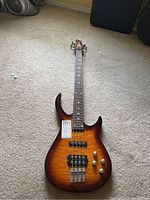 Full body image of Rogue Series 3 electric bass guitar lying on carpet showing its sunburst finish, four strings, and control knobs.